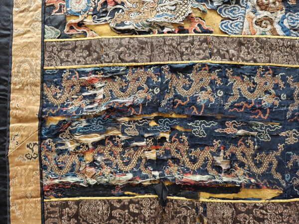 Distressed textile showing horizontal bands of embroidered golden dragons on dark blue, bordered by tan and brown fabric.