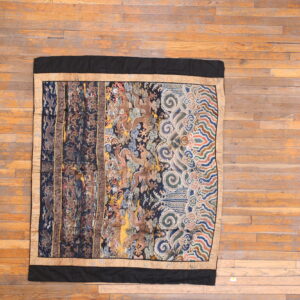 Intricate, multicolored textile featuring mythological patterns and borders displayed on plank hardwood flooring.