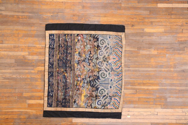 Intricate, multicolored textile featuring mythological patterns and borders displayed on plank hardwood flooring.