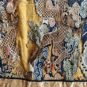 Heavily damaged yellow, blue, and gold textile fragment with high-texture embroidery depicting dragon scales and clouds.