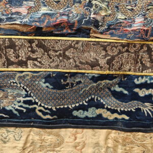Close-up shows layered textiles: gold and blue dragon weave, brown patterned fabric, and textured beige cloth.