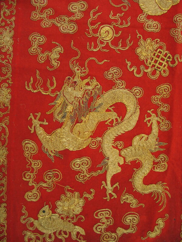 Red textile detailed with a gold embroidered dragon, swirling clouds, and traditional floral patterns.