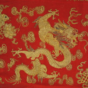 A close-up of a red rug featuring dense golden thread forming dragon, fish, and cloud motifs.