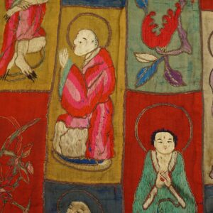 Embroidered textile with red, gold, and teal patchwork panels showing stylized religious figures and floral motifs.