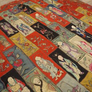 Flat, colorful patchwork rug with embroidered figures and flowers displayed on light wooden flooring.
