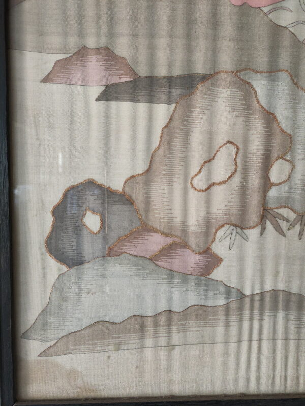 Pale woven textile framed behind glass, featuring abstract shapes in muted gray, pink, and copper outlines.