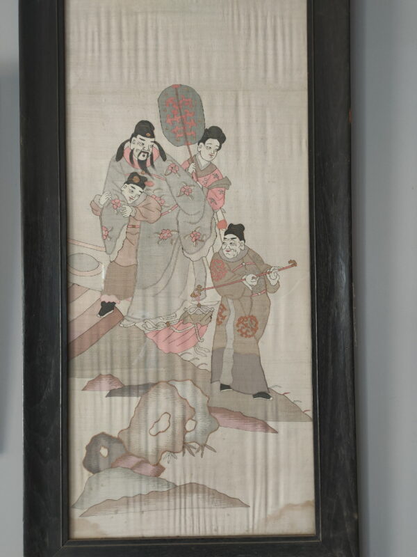 Woven textile art depicting four figures in muted pink and gray robes, enclosed in a dark frame.