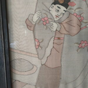 Flat-woven textile in gray, pink, and cream, depicting a framed figure holding pink floral elements.