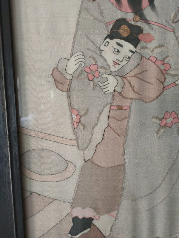Flat-woven textile in gray, pink, and cream, depicting a framed figure holding pink floral elements.