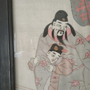 Textured textile artwork of two robed figures with pink flowers within a dark frame.