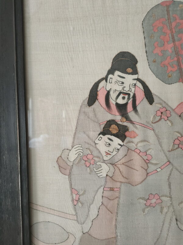 Textured textile artwork of two robed figures with pink flowers within a dark frame.