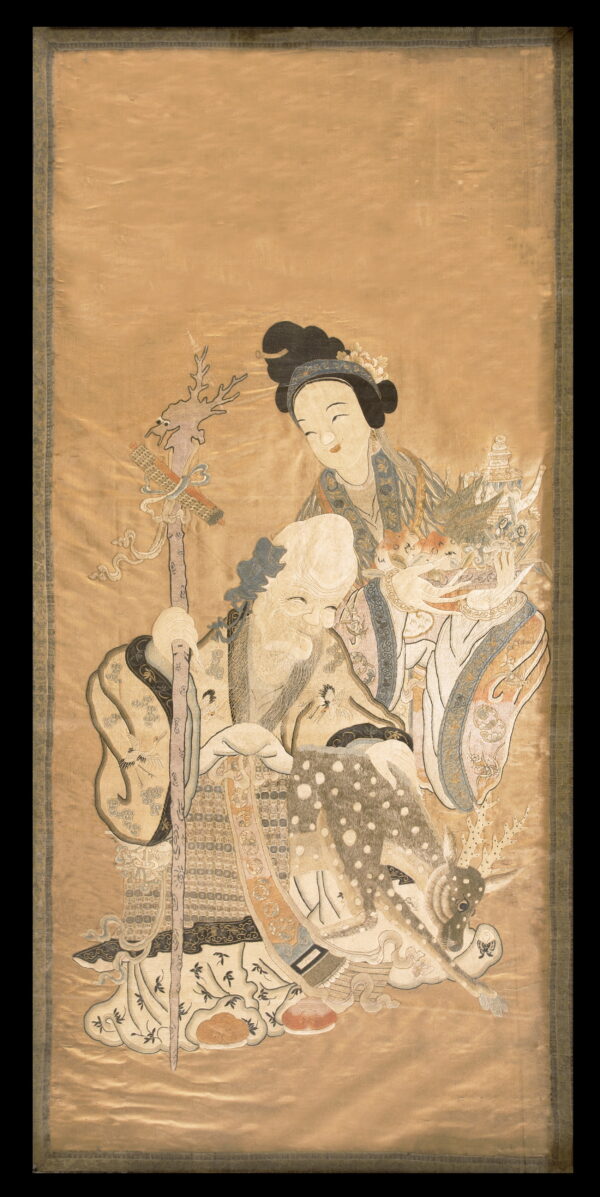 An intricate embroidered textile scroll featuring a smiling old man, a young woman, and a spotted fawn.