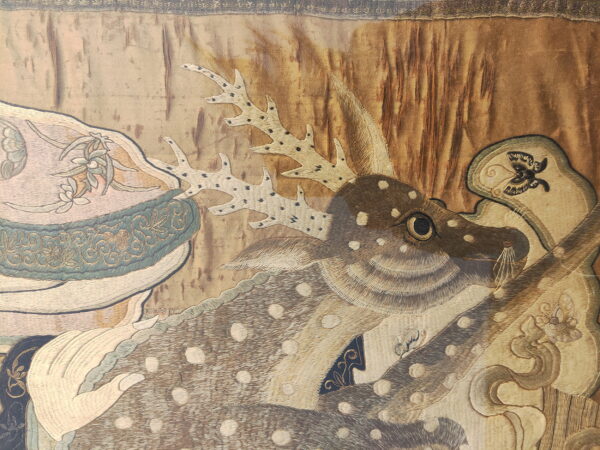 Detailed embroidery shows a spotted deer and antlers against a gold background with teal and cream figurative accents.