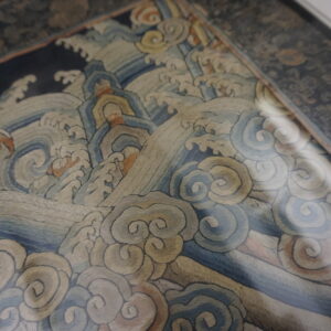 Tightly woven textile detail featuring traditional stylized waves in muted blue, tan, and rust colors.