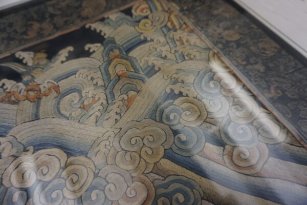 Tightly woven textile detail featuring traditional stylized waves in muted blue, tan, and rust colors.