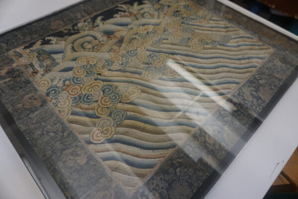 Ornate rug sample displaying a central diamond pattern of waves and clouds with a dark floral border.