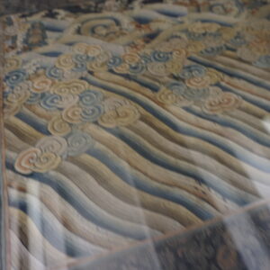 Muted rug displaying horizontal wavy lines, cloud motifs in pale blue and cream, and a dark patterned border.