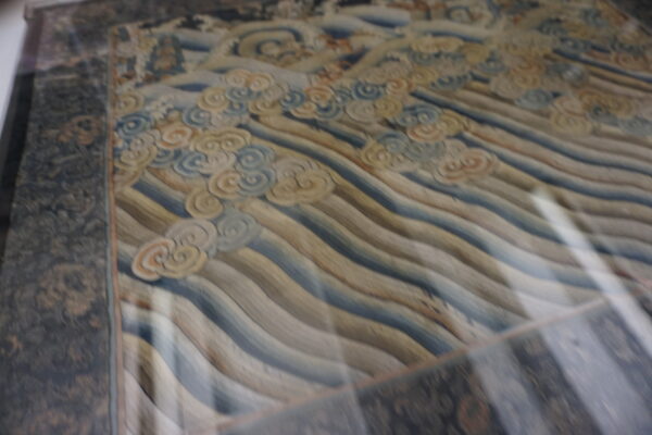 Muted rug displaying horizontal wavy lines, cloud motifs in pale blue and cream, and a dark patterned border.