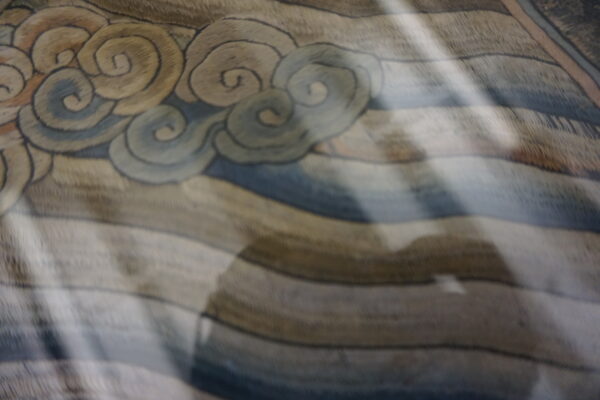 Muted beige and blue cloud-patterned rug texture with strong diagonal light and a large central shadow.