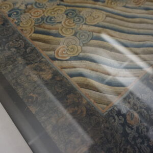 Detailed view of a framed textile with a cloudy, wavy center and a distressed dark dark gray border.