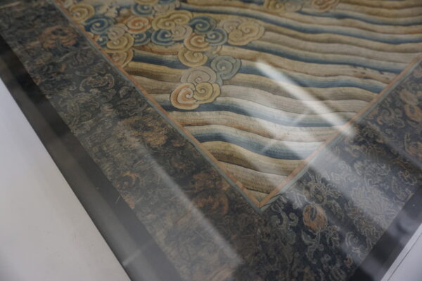 Detailed view of a framed textile with a cloudy, wavy center and a distressed dark dark gray border.