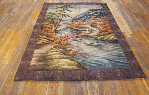 Scenic rug with a river, bridge, and autumn foliage bordered by dark brown pattern on wood floor.