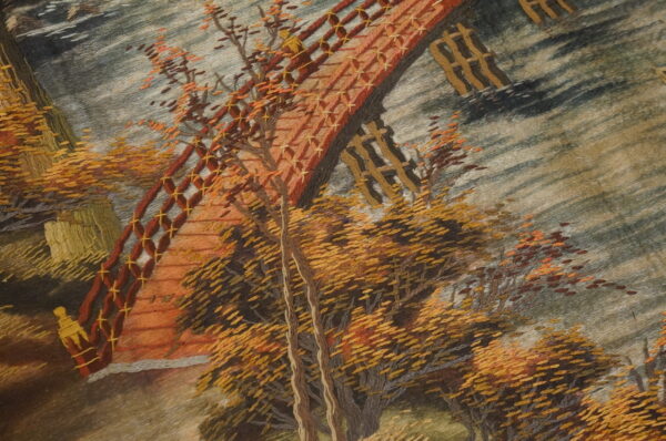 Close-up of a textured scenic rug depicting an autumn bridge and thick yellow and orange trees.