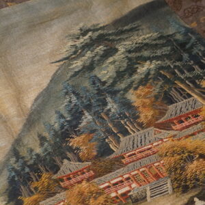 Textured textile featuring a mountainous scene with dense blue trees, orange foliage, and tiered red buildings.