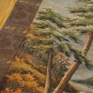 A detailed low-pile scenic rug depicting green trees and a brown border rests on yellow wooden flooring.