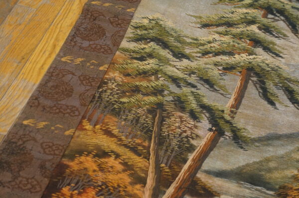A detailed low-pile scenic rug depicting green trees and a brown border rests on yellow wooden flooring.