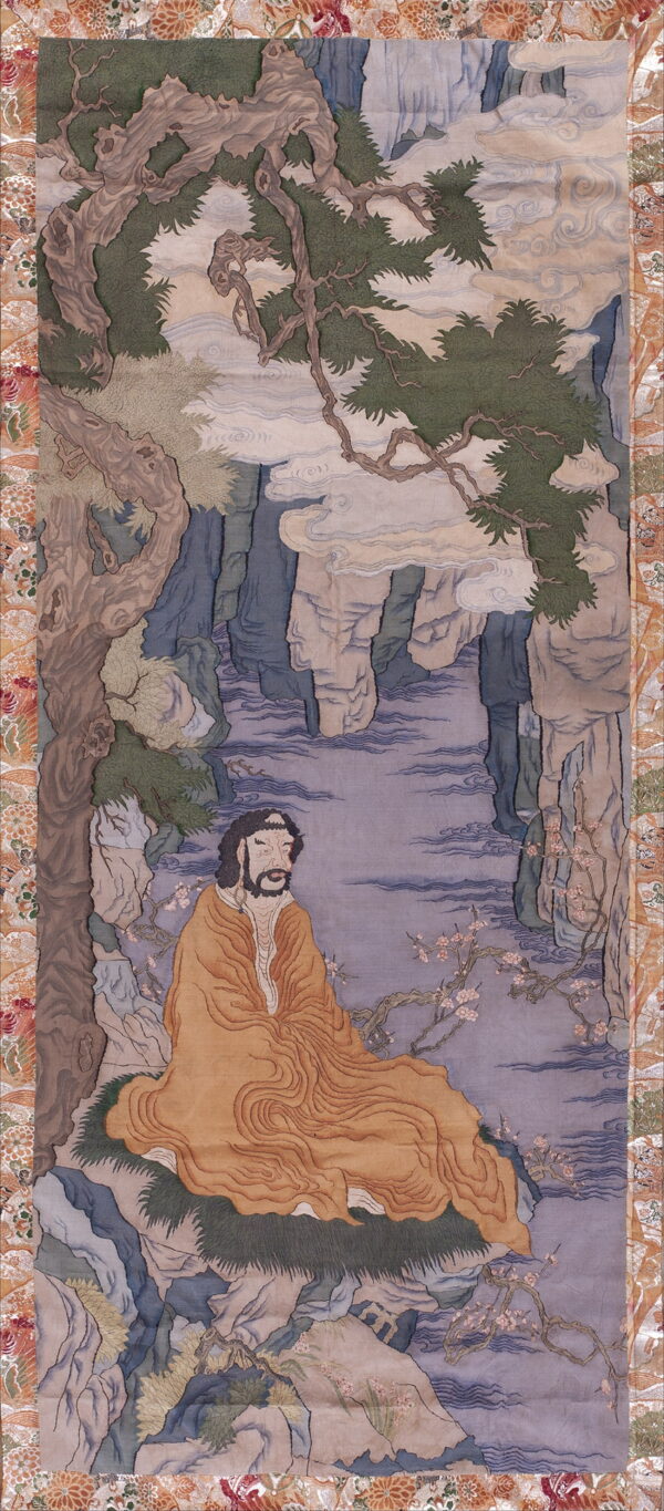 Low-pile rug depicting a bearded figure in orange robes surrounded by blue cliffs and and green pine trees.