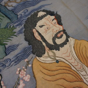 Intricate flat-weave rug featuring a figure in a brown robe, pink blossoms, green trees, and blue wavy patterns.