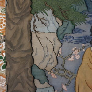 Figural tapestry detail shows a bearded man, green foliage, and pink blossoms beside a patterned orange textile.