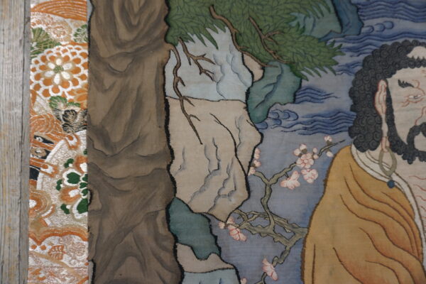 Figural tapestry detail shows a bearded man, green foliage, and pink blossoms beside a patterned orange textile.