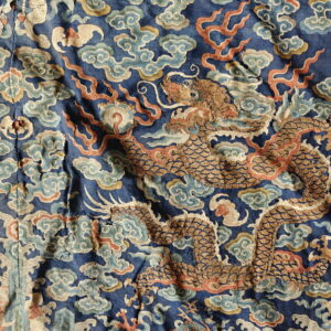Close-up of a blue woven textile showing a gold dragon pattern among colorful clouds and flame motifs.