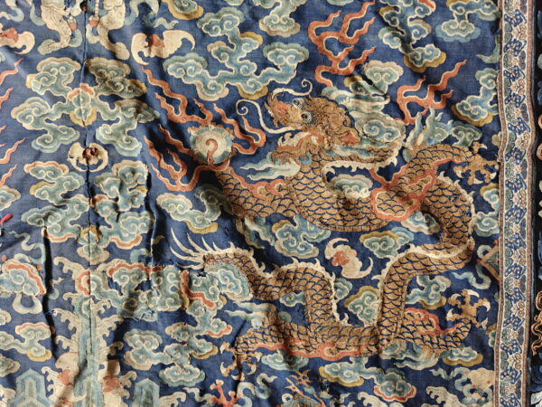 Close-up of a blue woven textile showing a gold dragon pattern among colorful clouds and flame motifs.