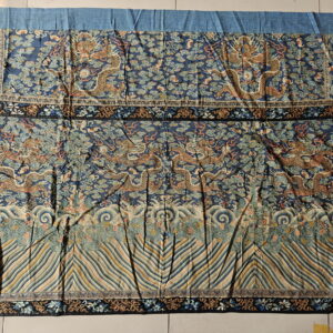 Blue embroidered textile displaying gold dragons, stylized clouds, and striped wave patterns on a tile floor.