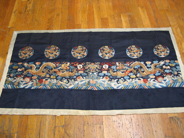 Dark blue textile with embroidered golden dragons and wave patterns lies flat on light brown wood planks.