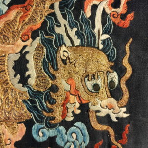 Close view of a black rug with a detailed gold, orange, and blue embroidered dragon pattern.
