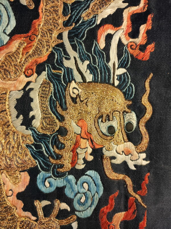 Close view of a black rug with a detailed gold, orange, and blue embroidered dragon pattern.