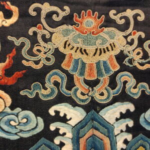 Intricate detail of a dark rug featuring multi-colored patterns including clouds, waves, and a stylized mask motif.
