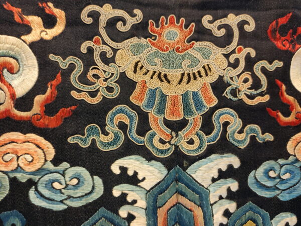 Intricate detail of a dark rug featuring multi-colored patterns including clouds, waves, and a stylized mask motif.