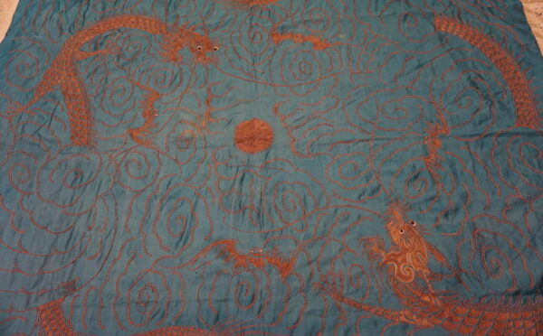 Flat teal textile featuring a rust-orange pattern of dragons, swirling clouds, and a central orb.