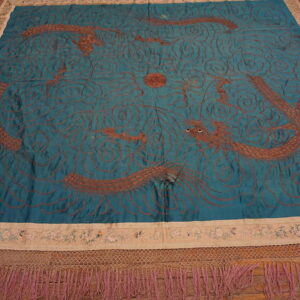 Square teal textile featuring copper-colored embroidered dragons, wide beige floral borders, and heavy magenta fringe.