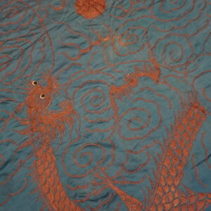 A close-up shows rusty brown dragons and cloud patterns against a wrinkled teal background.