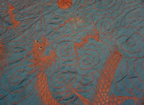 A close-up shows rusty brown dragons and cloud patterns against a wrinkled teal background.