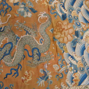 Detail of a textile with embroidered green dragon, vibrant blue waves, and large yellow flowers on a shimmering gold ground.