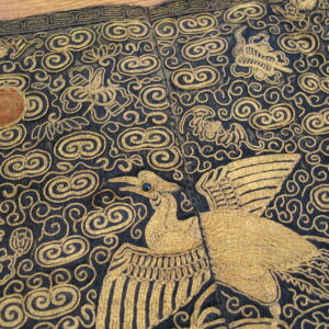 Gold metallic embroidery details a stylized bird and dense swirling clouds on a dark navy background.