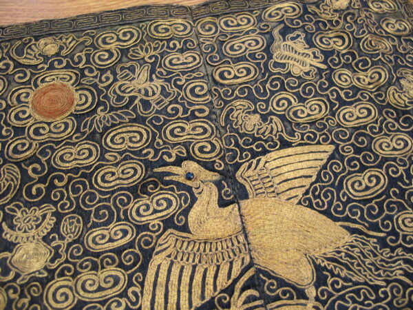 Gold metallic embroidery details a stylized bird and dense swirling clouds on a dark navy background.