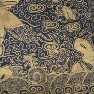 Raised gold embroidery forms intricate scrollwork and animal motifs on a dark textile over wood flooring.